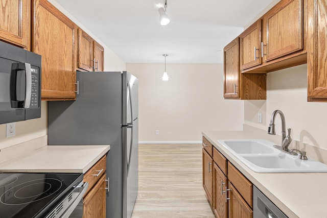 kitchen with sink, appliances with stainless steel finishes, hanging light fixtures, and light hardwood / wood-style floors