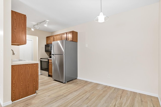 kitchen featuring rail lighting, light wood-type flooring, stainless steel appliances, pendant lighting, and sink