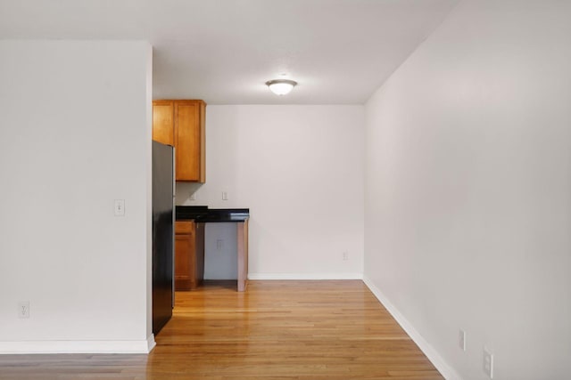 kitchen featuring light wood finished floors, dark countertops, brown cabinetry, freestanding refrigerator, and baseboards