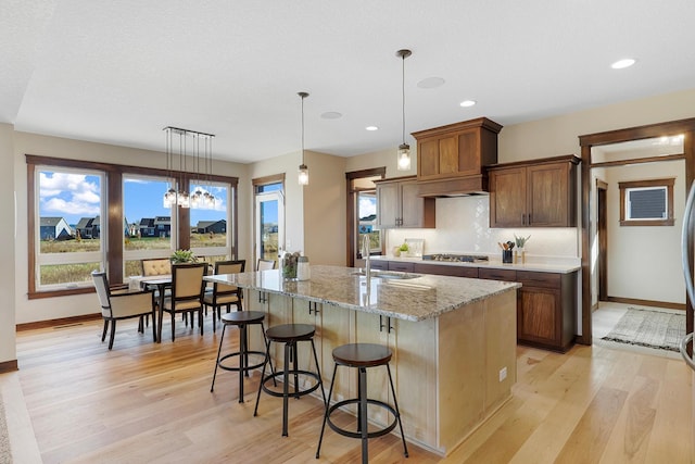 kitchen with an island with sink, sink, light stone countertops, decorative light fixtures, and light hardwood / wood-style floors