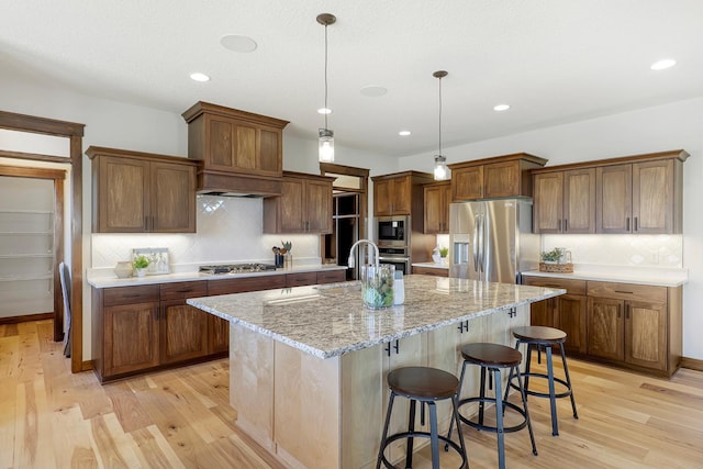 kitchen with a center island with sink, stainless steel appliances, and light wood-type flooring