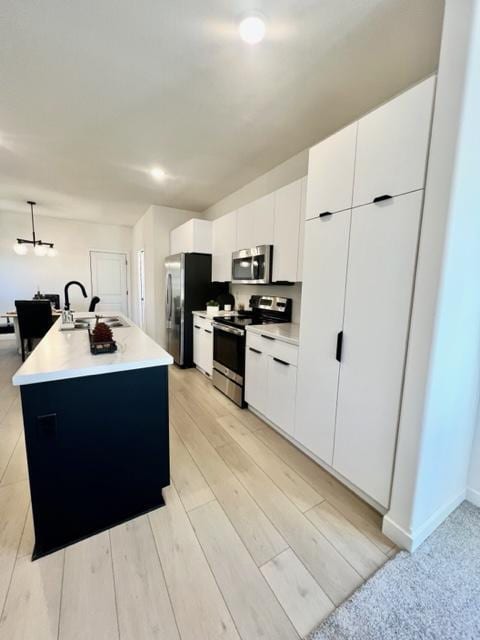 kitchen featuring sink, an island with sink, white cabinetry, light hardwood / wood-style floors, and stainless steel appliances