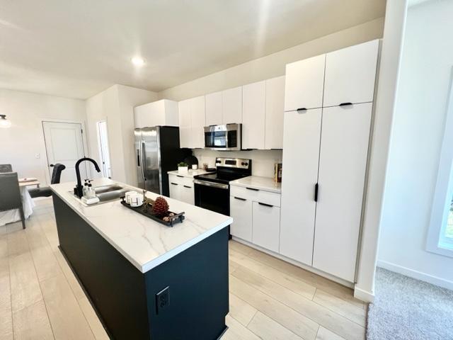 kitchen with appliances with stainless steel finishes, light hardwood / wood-style flooring, white cabinetry, and a center island with sink