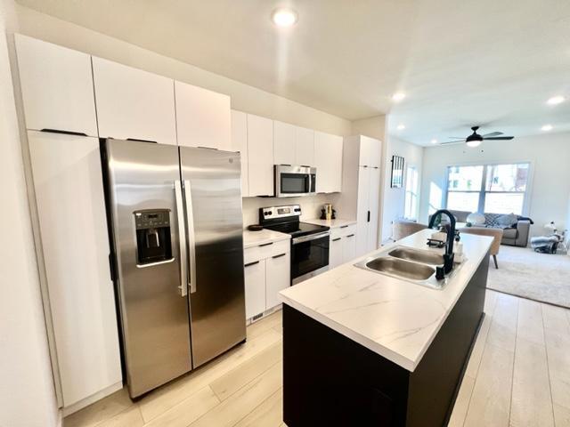 kitchen with light hardwood / wood-style flooring, a center island with sink, sink, white cabinets, and appliances with stainless steel finishes