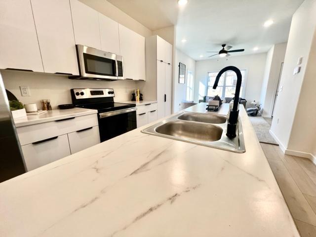 kitchen with appliances with stainless steel finishes, white cabinets, sink, and light hardwood / wood-style floors