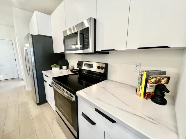 kitchen with appliances with stainless steel finishes, white cabinets, and light stone countertops