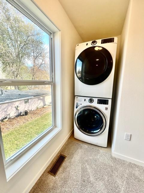 washroom with stacked washing maching and dryer, a healthy amount of sunlight, and carpet floors