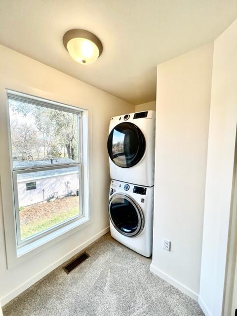 laundry area with stacked washer / drying machine, light colored carpet, and a healthy amount of sunlight