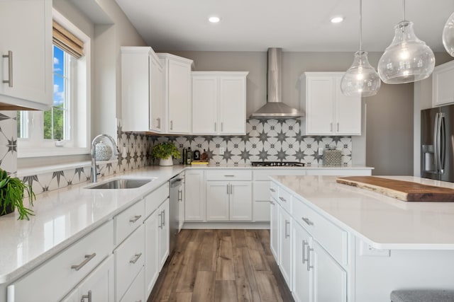 kitchen with wall chimney range hood, dark wood-type flooring, sink, decorative light fixtures, and white cabinets