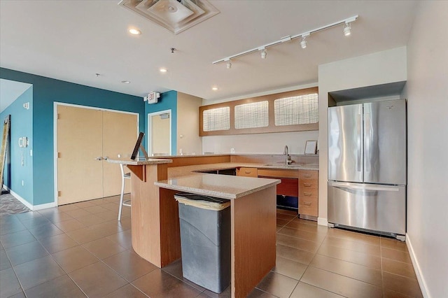 kitchen with stainless steel refrigerator, light stone counters, dark tile patterned floors, kitchen peninsula, and a breakfast bar