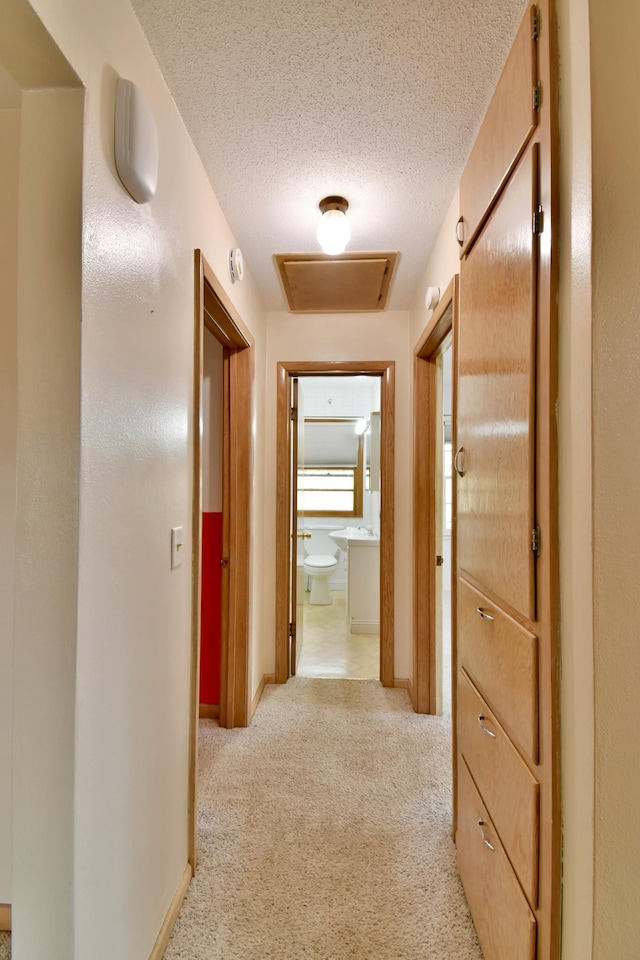 hallway with light colored carpet and a textured ceiling