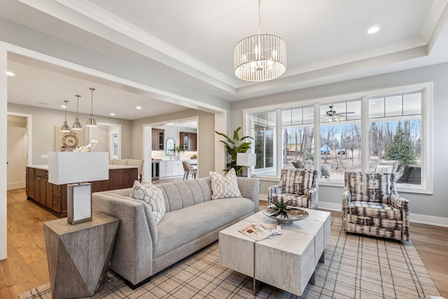 living room with crown molding, light hardwood / wood-style flooring, a tray ceiling, and an inviting chandelier