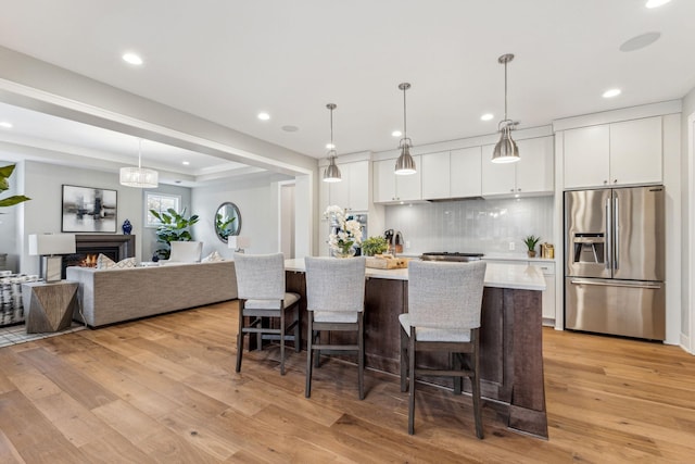 kitchen featuring white cabinetry, light hardwood / wood-style floors, hanging light fixtures, and stainless steel fridge