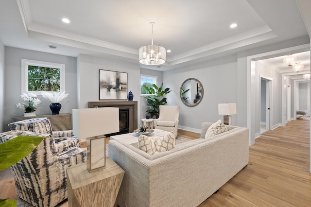 living room featuring a chandelier, crown molding, light wood-type flooring, and a raised ceiling