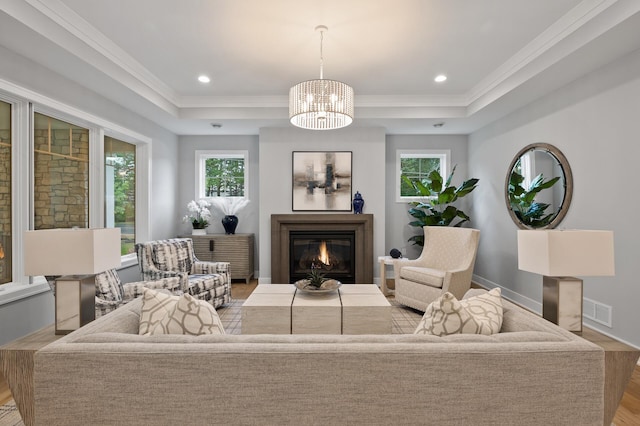 living room with an inviting chandelier, crown molding, light wood-type flooring, and a raised ceiling