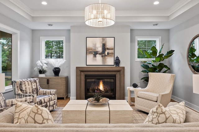 living area featuring ornamental molding, a chandelier, a tray ceiling, and light wood-type flooring