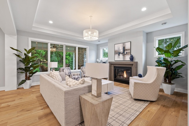 living room featuring light hardwood / wood-style flooring, ornamental molding, a chandelier, and a tray ceiling