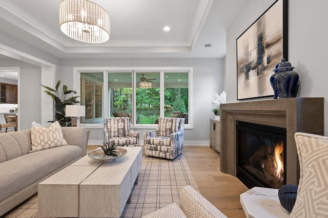 living room with a tray ceiling, ornamental molding, light hardwood / wood-style flooring, and an inviting chandelier