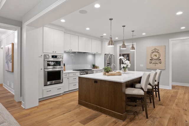 kitchen with appliances with stainless steel finishes, light hardwood / wood-style flooring, hanging light fixtures, and a center island with sink