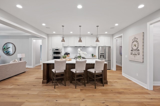 kitchen featuring hanging light fixtures, a large island with sink, a kitchen breakfast bar, light wood-type flooring, and stainless steel appliances