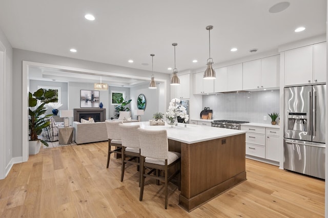 kitchen with white cabinetry, a kitchen island with sink, light hardwood / wood-style flooring, pendant lighting, and stainless steel appliances