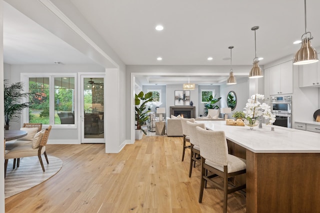 kitchen with stainless steel double oven, light stone countertops, pendant lighting, light wood-type flooring, and white cabinetry