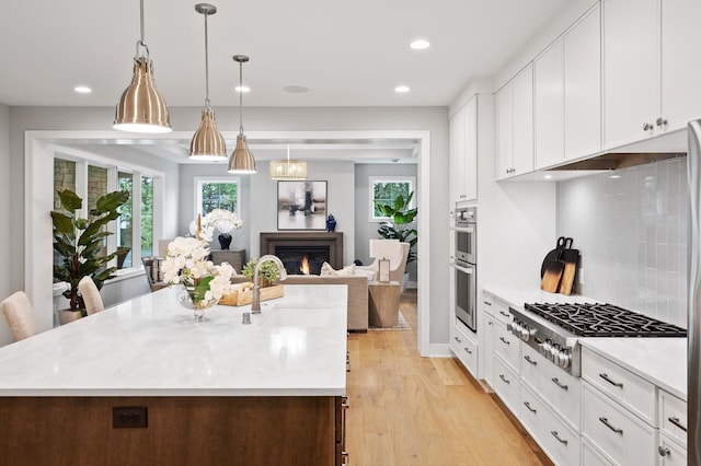 kitchen with light hardwood / wood-style floors, white cabinetry, appliances with stainless steel finishes, and a center island with sink