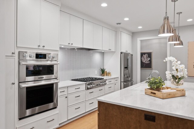 kitchen featuring light hardwood / wood-style flooring, stainless steel appliances, backsplash, decorative light fixtures, and white cabinetry