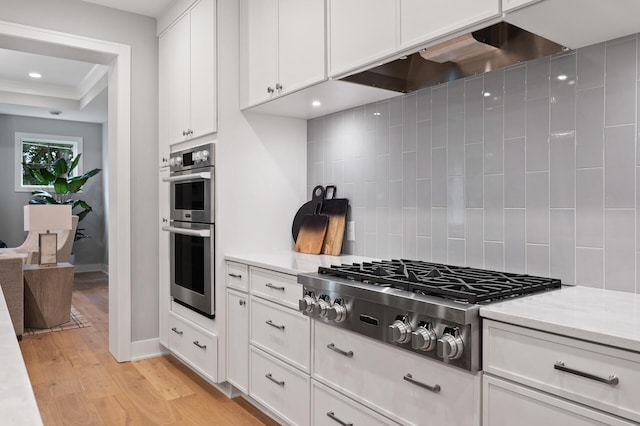 kitchen featuring tasteful backsplash, light wood-type flooring, stainless steel appliances, white cabinets, and ventilation hood