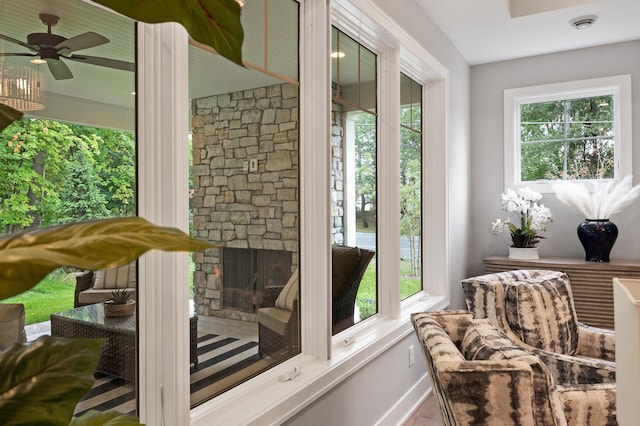 sunroom / solarium featuring a stone fireplace and ceiling fan