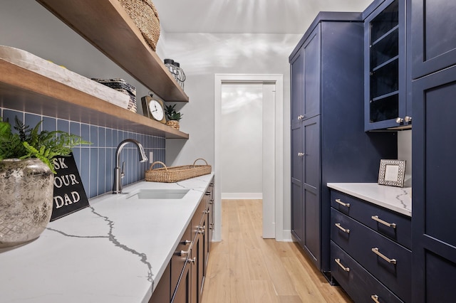 kitchen with light hardwood / wood-style floors, light stone countertops, sink, and blue cabinetry