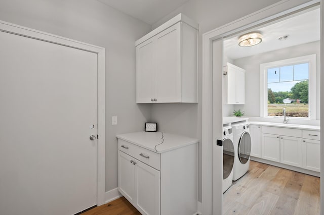 clothes washing area featuring sink, washing machine and dryer, light wood-type flooring, and cabinets