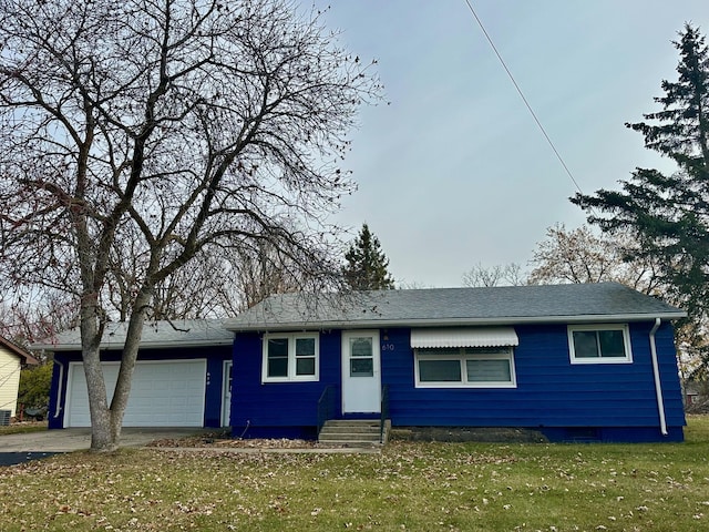 ranch-style home with a garage, entry steps, concrete driveway, roof with shingles, and a front lawn