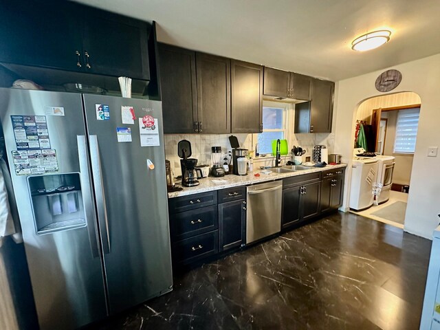 kitchen with arched walkways, appliances with stainless steel finishes, a sink, washing machine and dryer, and backsplash