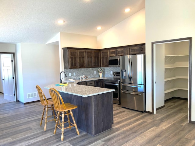 1067 241st Ln NE, East Bethel, MN 55005 - kitchen featuring stainless steel appliances, dark brown cabinets, a peninsula, decorative backsplash, and a kitchen bar