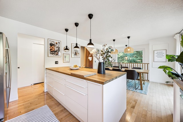 kitchen featuring white cabinets, decorative light fixtures, light wood-type flooring, and butcher block countertops