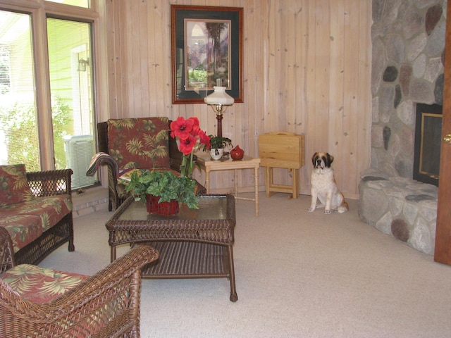 living area featuring wood walls, a stone fireplace, and carpet flooring