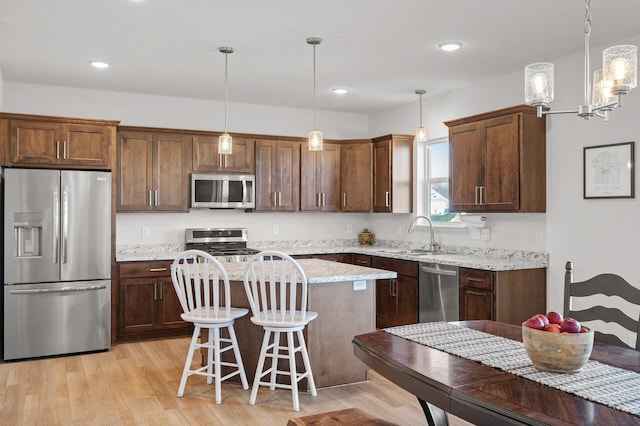 kitchen with light hardwood / wood-style floors, stainless steel appliances, a center island, sink, and decorative light fixtures