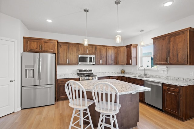 kitchen with stainless steel appliances, sink, a kitchen island, light hardwood / wood-style flooring, and decorative light fixtures