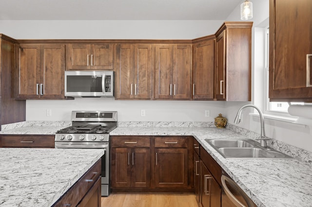 kitchen with light wood-type flooring, appliances with stainless steel finishes, sink, and light stone countertops