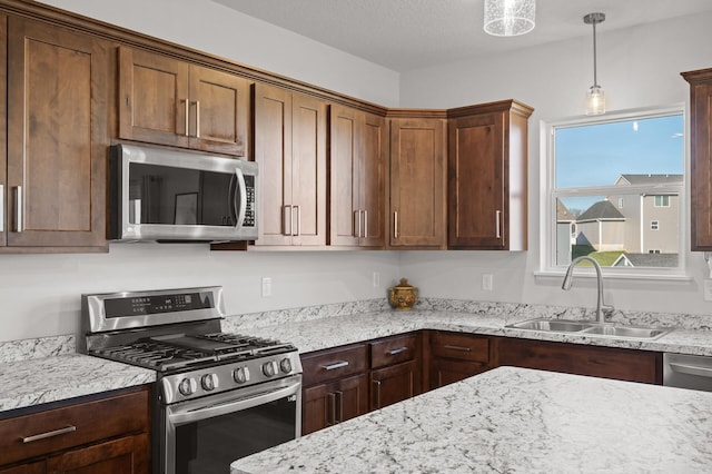 kitchen with stainless steel appliances, sink, light stone countertops, a textured ceiling, and hanging light fixtures