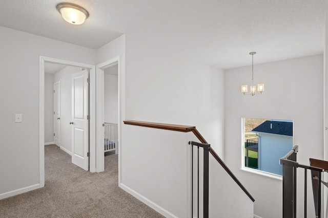 hallway featuring light colored carpet, a textured ceiling, and a chandelier