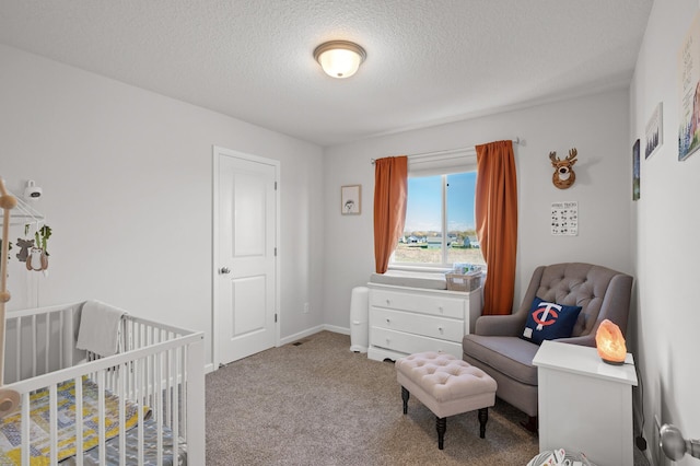 bedroom with a crib, a textured ceiling, and carpet floors