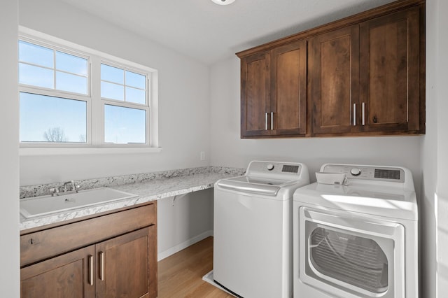 clothes washing area with cabinets, washing machine and dryer, sink, and light hardwood / wood-style flooring