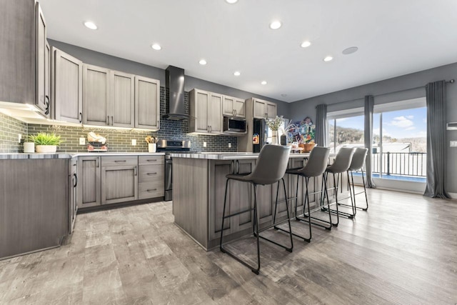 kitchen featuring a breakfast bar area, appliances with stainless steel finishes, a kitchen island, light wood-type flooring, and wall chimney exhaust hood