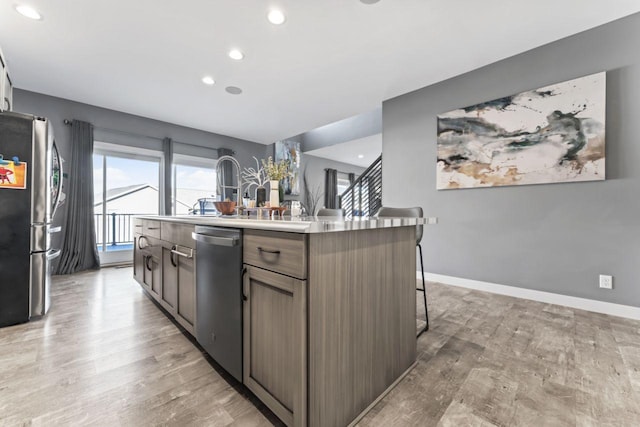 kitchen featuring light wood-type flooring, stainless steel appliances, a breakfast bar, and an island with sink