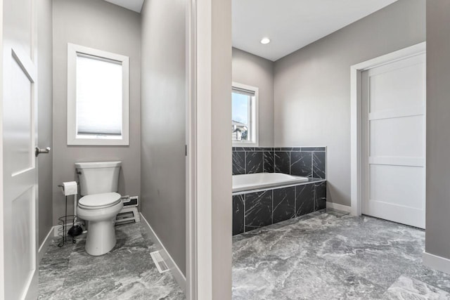 bathroom featuring toilet and a relaxing tiled tub