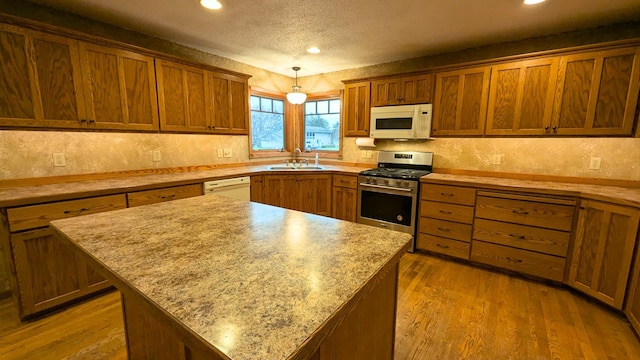 kitchen featuring a kitchen island, a sink, a textured ceiling, wood finished floors, and white appliances