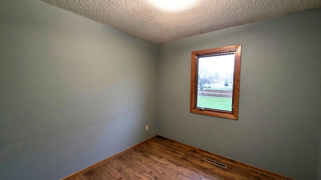 empty room with a textured ceiling, wood finished floors, visible vents, and baseboards