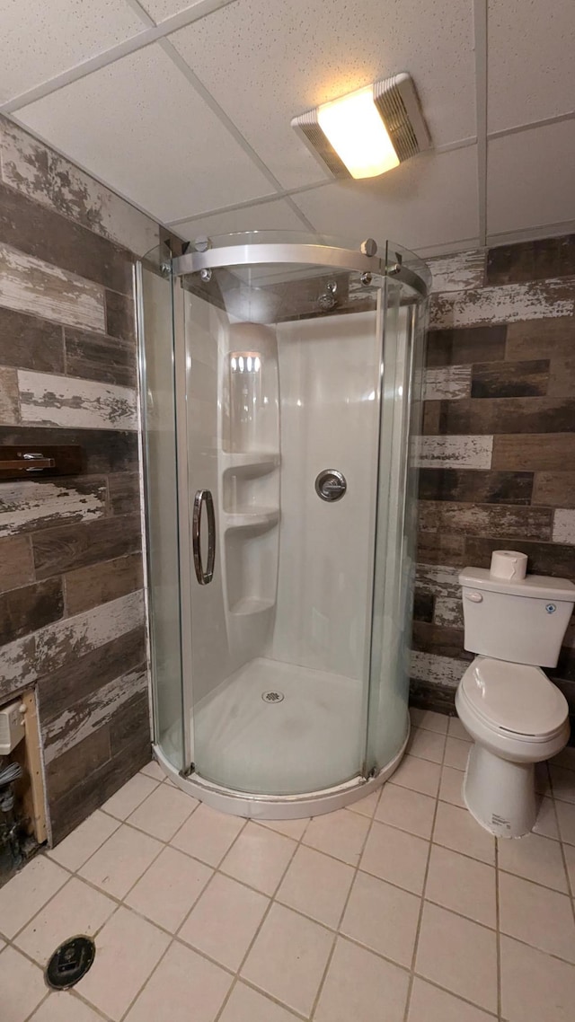 full bath featuring toilet, a stall shower, wooden walls, and tile patterned floors